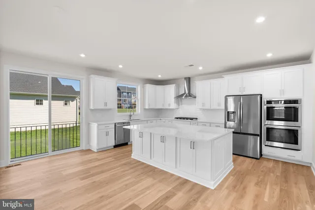 a kitchen with stainless steel appliances kitchen island granite countertop a refrigerator oven a sink dishwasher and white cabinets with wooden floor