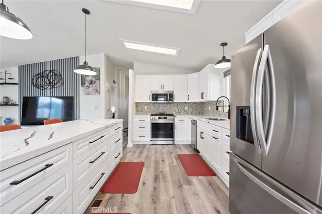 a kitchen with stainless steel appliances granite countertop a refrigerator a oven and white cabinets with wooden floor