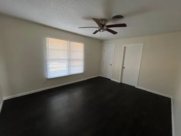 an empty room with wooden floor fan and windows