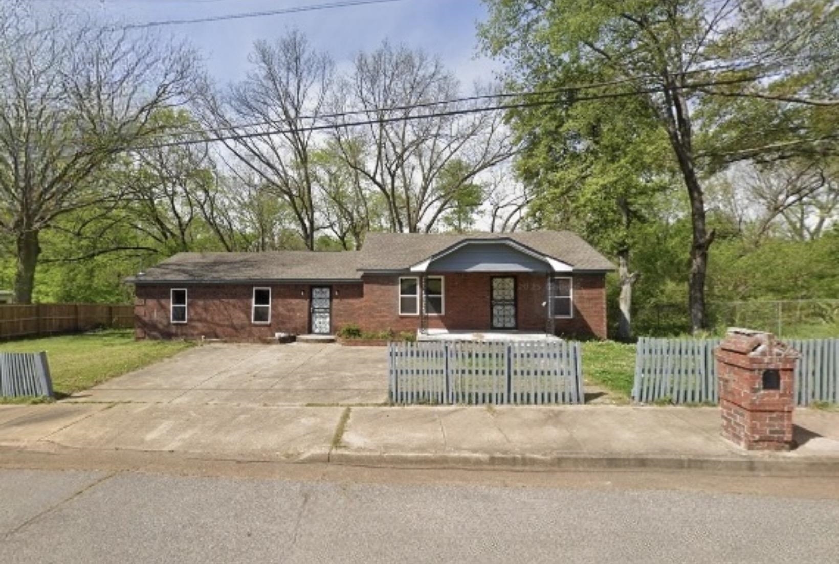 Brick exterior residence with a partial picket fence, concrete driveway, and a covered front entry