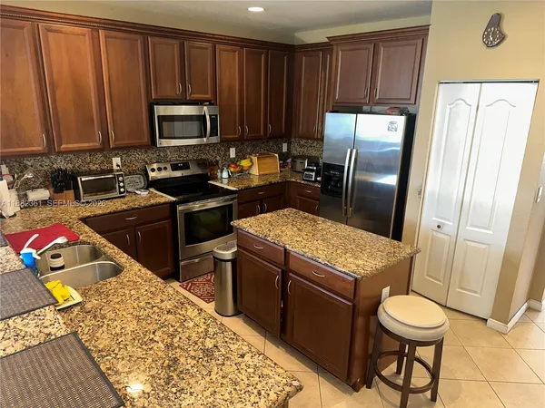 a kitchen with stainless steel appliances granite countertop a refrigerator stove top oven dining table and chairs