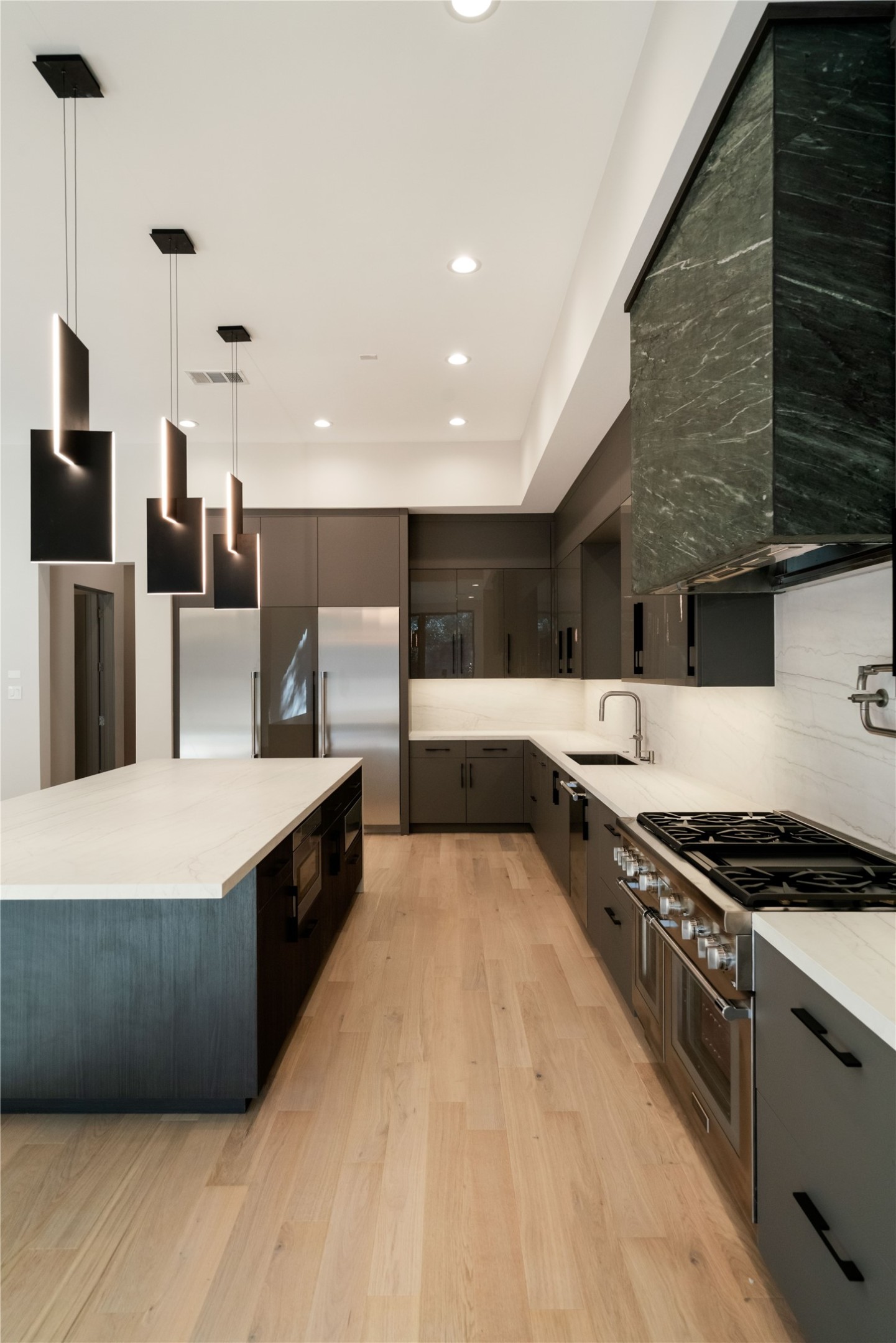 47 Pronghorn Place Spring, TX 77389 - Photo 11 of 44 This modern kitchen features sleek black cabinetry, a spacious island with pendant lighting, stainless steel appliances, and elegant hardwood flooring. The design offers ample counter space and a minimalist aesthetic.