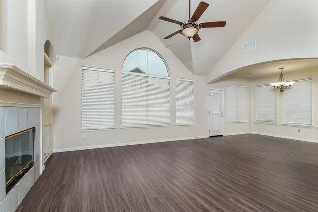 an empty room with wooden floor a ceiling fan a fireplace and windows