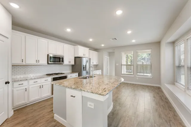 a kitchen with stainless steel appliances granite countertop a stove a sink dishwasher a refrigerator and white cabinets with wooden floor