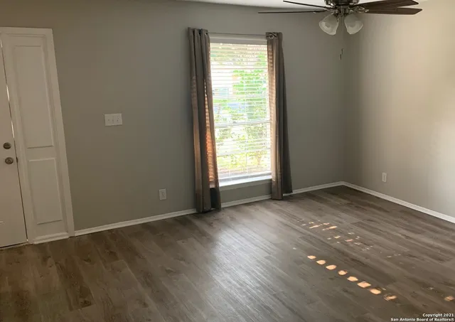 an empty room with wooden floor fan and windows