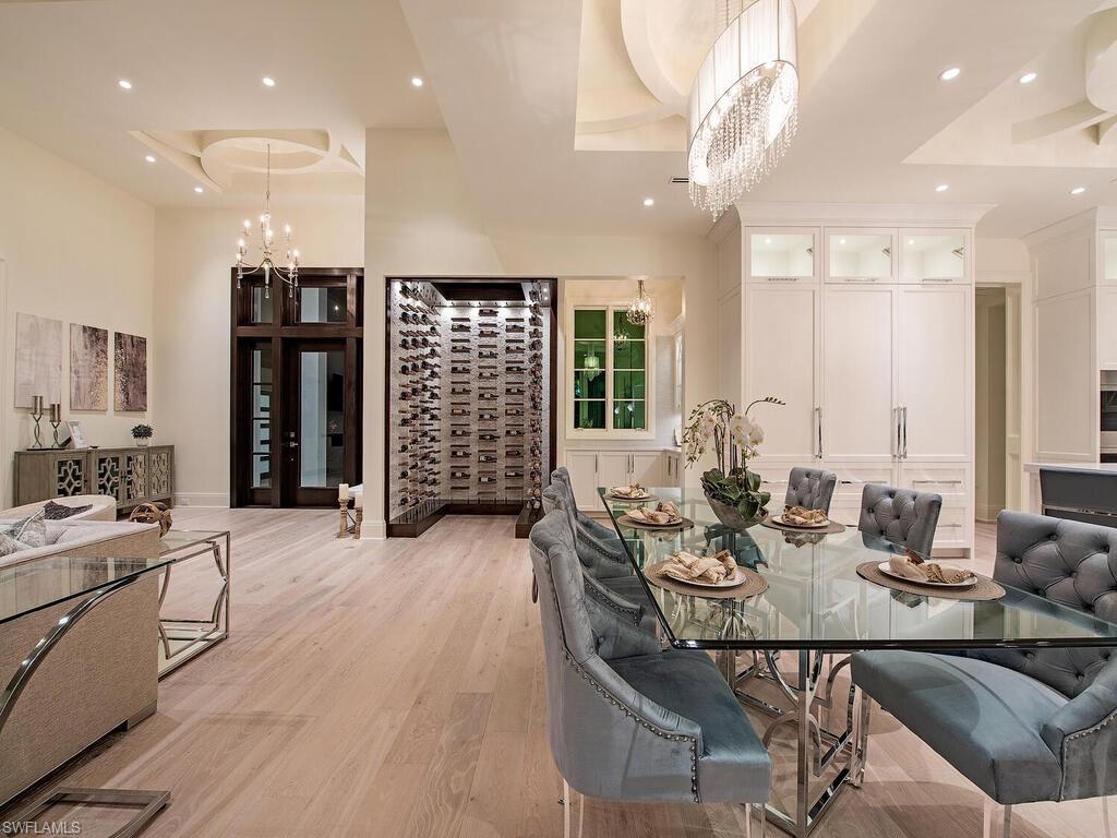 714 Killdeer Place Naples, FL 34108 - Photo 33 of 34 a view of a dining room and livingroom with furniture wooden floor a rug a flat screen tv a painting and a chandelier
