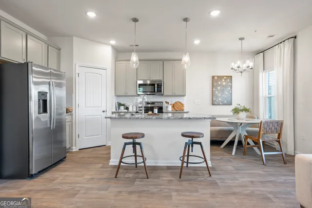 a kitchen with stainless steel appliances granite countertop a refrigerator a stove a sink a dining table and chairs with wooden floor