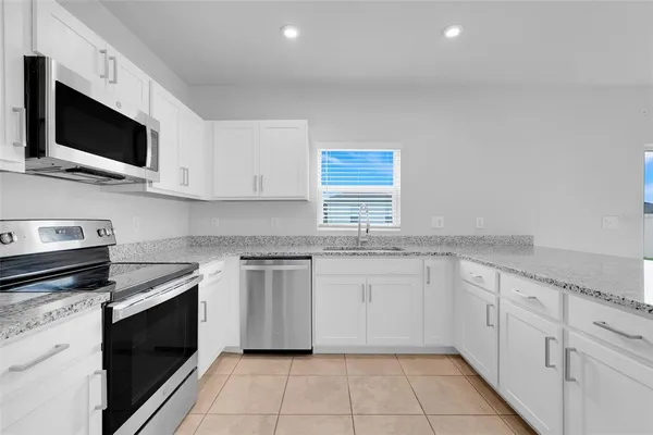 a kitchen with stainless steel appliances granite countertop a sink and a stove top oven with white cabinets