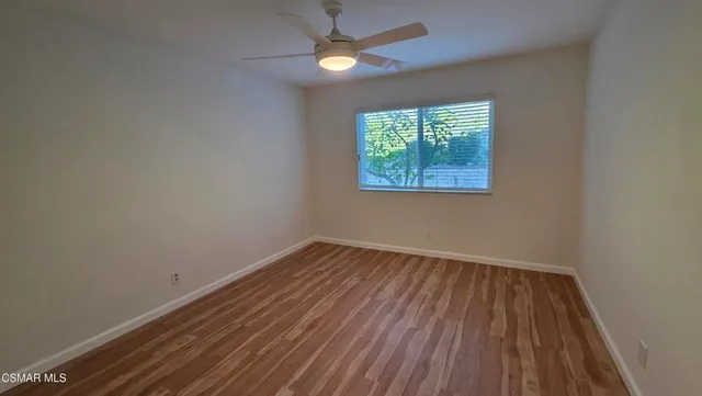 an empty room with wooden floor ceiling fan and windows