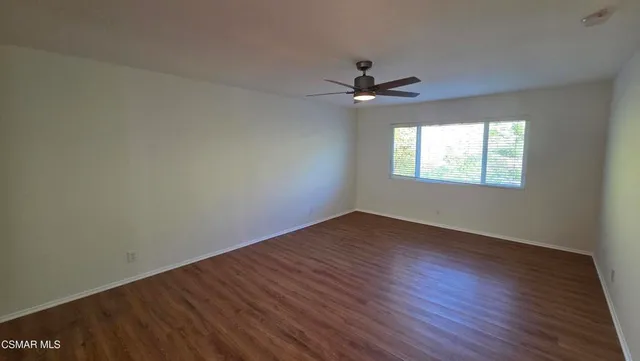 an empty room with wooden floor fan and windows