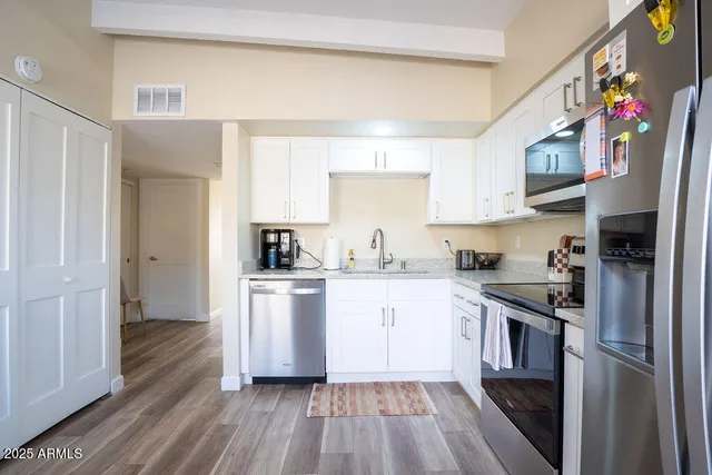 a kitchen with stainless steel appliances granite countertop a refrigerator a sink dishwasher a stove and white countertops with wooden floor