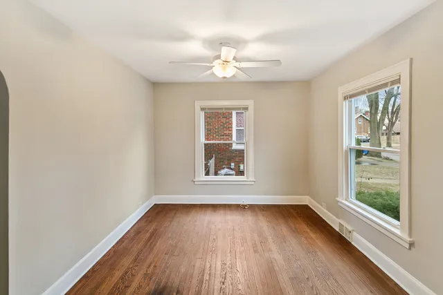 an empty room with wooden floor chandelier fan and windows