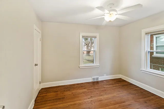 an empty room with wooden floor ceiling fan and windows