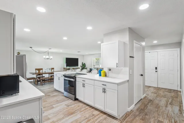 a kitchen with stainless steel appliances a stove top oven a sink a refrigerator white wooden cabinets and couches