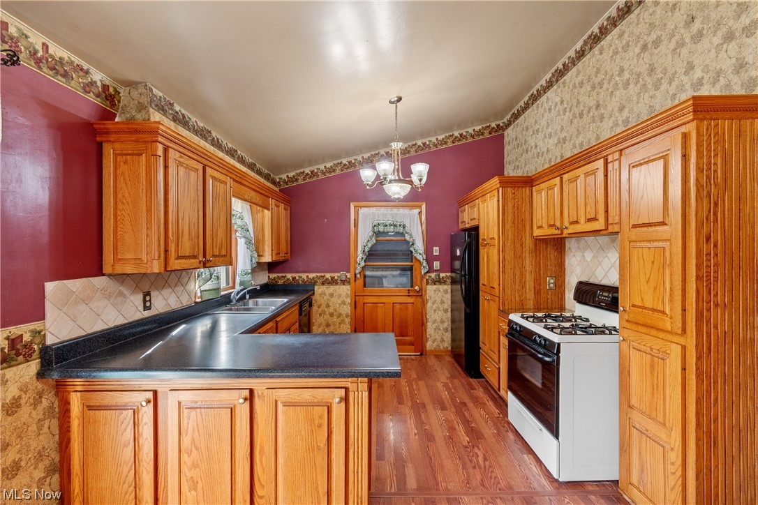 120 Lester Road New Franklin, OH 44319 - Photo 6 of 24 Kitchen with white gas range oven, dark countertops, brown cabinets, vaulted ceiling, light hardwood flooring, backsplash, and black fridge
