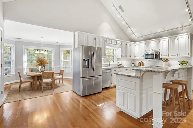 a kitchen with stainless steel appliances granite countertop a refrigerator a stove a sink a dining table and chairs with wooden floor