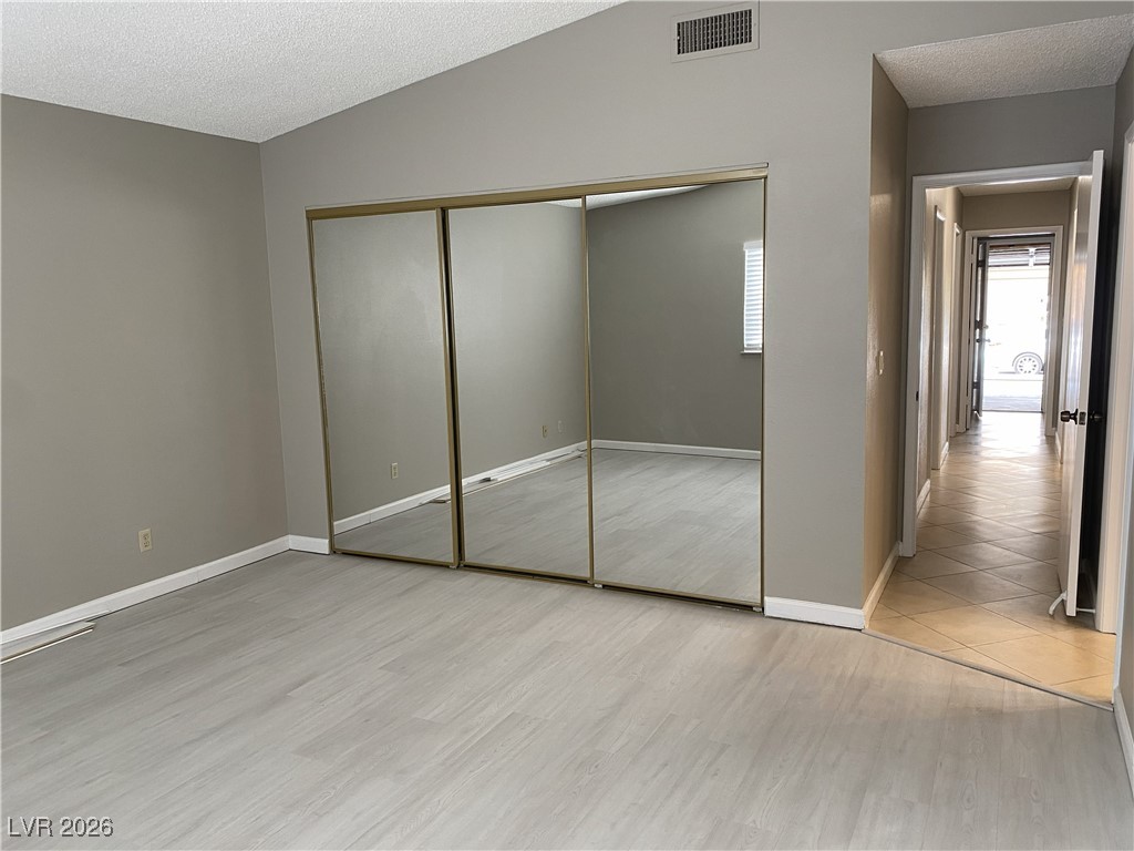 Undisclosed Address Las Vegas, NV 89108 - Photo 16 of 26 Unfurnished bedroom featuring vaulted ceiling, a textured ceiling, a closet, and light wood-style flooring