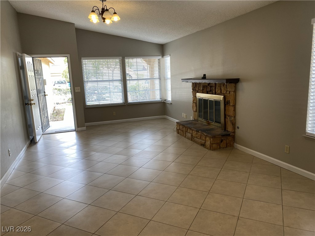 Undisclosed Address Las Vegas, NV 89108 - Photo 4 of 26 Unfurnished living room with a textured ceiling, light tile patterned floors, lofted ceiling, a stone fireplace, and a chandelier