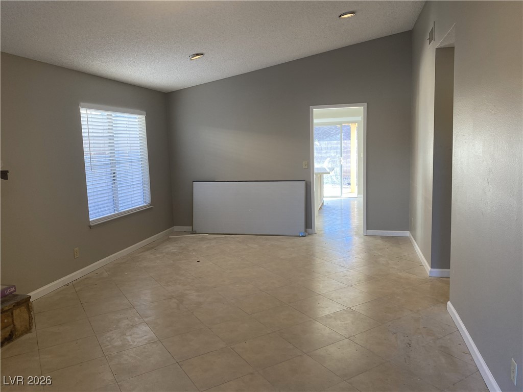 Undisclosed Address Las Vegas, NV 89108 - Photo 5 of 26 Empty room featuring a textured ceiling, lofted ceiling, healthy amount of natural light, and light tile patterned flooring