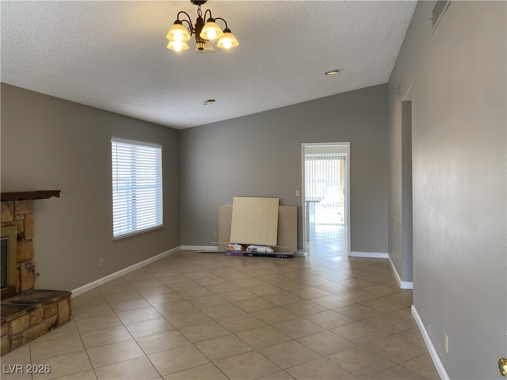 Undisclosed Address Las Vegas, NV 89108 - Photo 6 of 26 Unfurnished living room with light tile patterned floors, a textured ceiling, lofted ceiling, a chandelier, and a fireplace