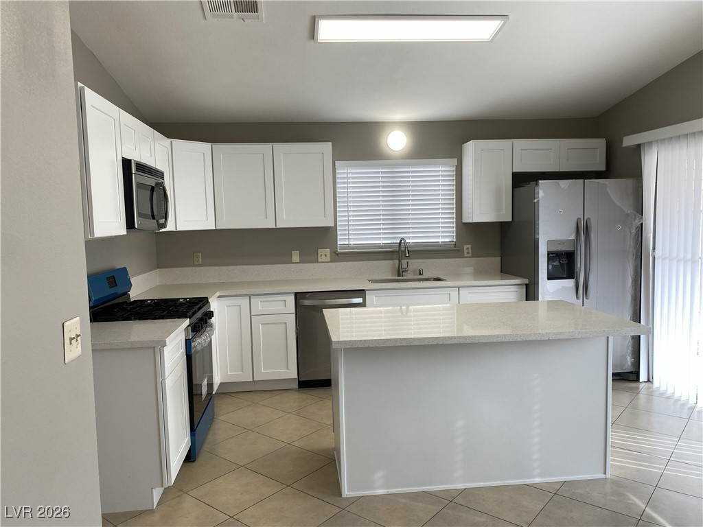 Undisclosed Address Las Vegas, NV 89108 - Photo 7 of 26 Kitchen with stainless steel appliances, vaulted ceiling, white cabinets, light tile patterned floors, and light stone countertops