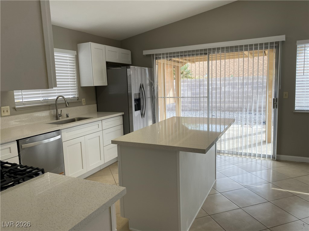 Undisclosed Address Las Vegas, NV 89108 - Photo 8 of 26 Kitchen with white cabinets, light tile patterned floors, stainless steel appliances, a kitchen island, and light stone counters