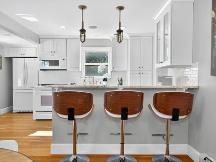 a very nice looking kitchen with granite countertop a stove a sink a kitchen island with white cabinets and wooden floor