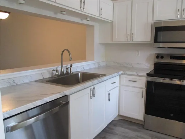 a kitchen with white cabinets a sink and a stove with wooden floor