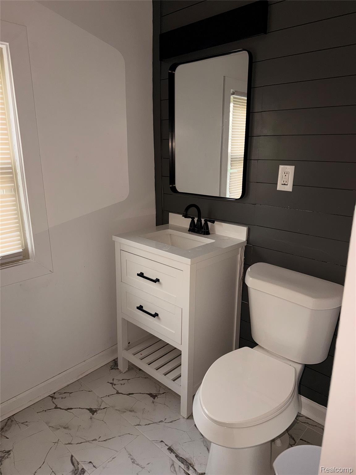 3914 Balfour Road Detroit, MI 48224 - Photo 8 of 24 White vanity with black hardware, rectangular mirror, black wall-mounted light fixture, white toilet, and marble-look floor tiles