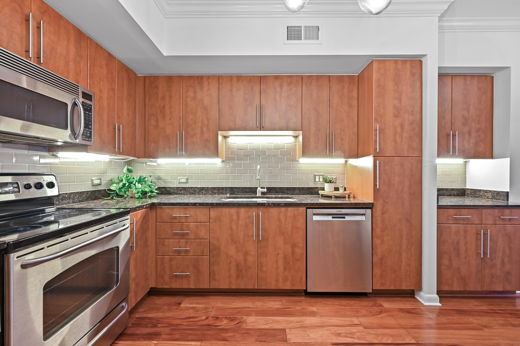 54 Rainey Street, Unit 412 Austin, TX 78701 - Photo 4 of 37 Kitchen with appliances with stainless steel finishes, under mount lighting, granite countertops, brown cabinetry, wood floors, and ornamental molding