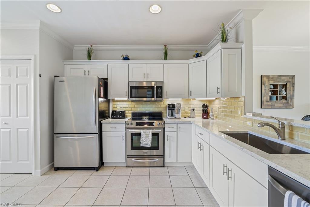 3047 Horizon Lane, Unit 1908 Naples, FL 34109 - Photo 4 of 17 Kitchen with white cabinetry, stainless steel appliances, light stone counters, sink, and light tile patterned flooring