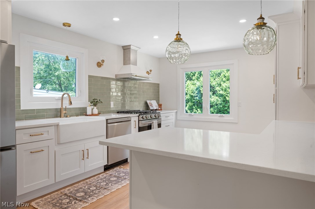 22625 Rye Road Shaker Heights, OH 44122 - Photo 10 of 38 Bright kitchen featuring white shaker cabinetry, light-toned countertops, a full subway tile backsplash, stainless steel appliances, and wood-finish flooring