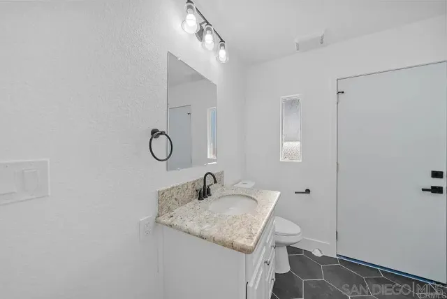 a bathroom with a granite countertop sink a toilet and with mirror