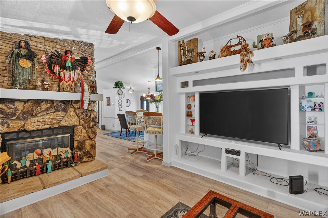 784 Pegasus Ranch Road Bullhead City, AZ 86429 - Photo 23 of 100 Living area featuring a stone fireplace with hearth, wood-finish flooring, a built-in media center with shelving, and a ceiling fan