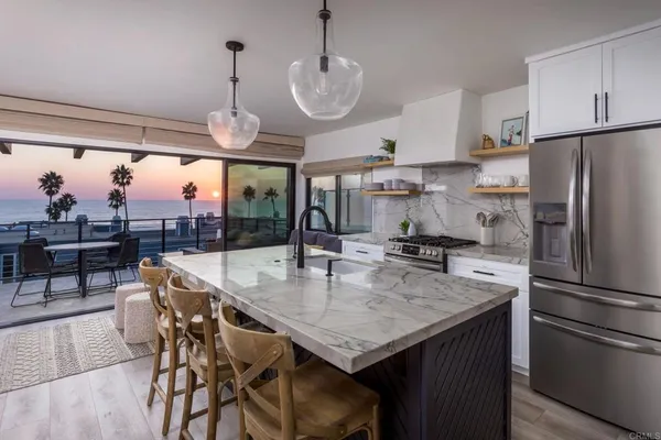 a kitchen with stainless steel appliances granite countertop a kitchen island a stove a refrigerator a oven a dining table and chairs with wooden floor