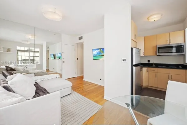 a living room with stainless steel appliances furniture a rug and a kitchen view