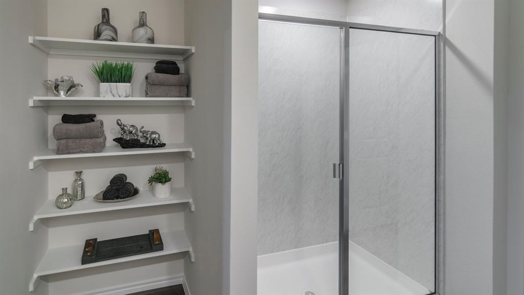3100 Charleston Drive Ennis, TX 75119 - Photo 15 of 23 Built-in shelving unit with multiple white shelves complemented by a shower enclosure featuring a white base and sliding frosted glass doors with metal framing
