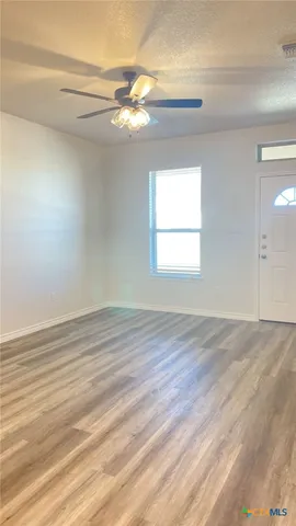 an empty room with wooden floor fan and windows