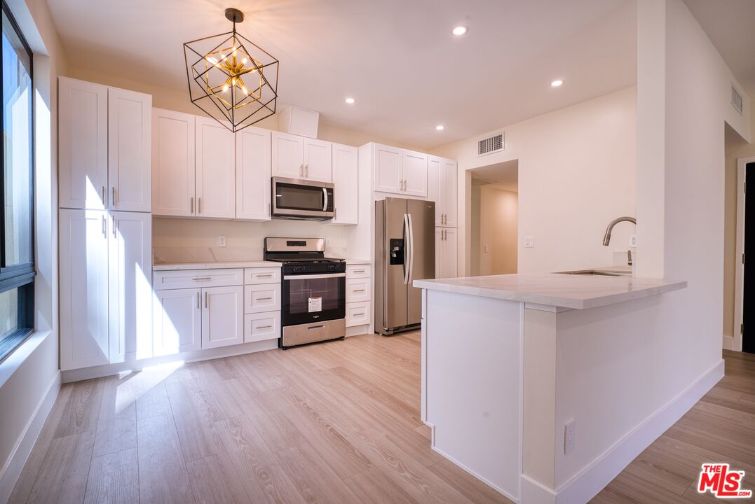 13920 Moorpark Street, Unit 201 Sherman Oaks, CA 91423 - Photo 6 of 25 a kitchen with kitchen island white cabinets stainless steel appliances and wooden floor