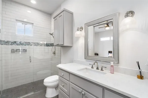 a bathroom with a granite countertop sink a toilet a mirror and shower