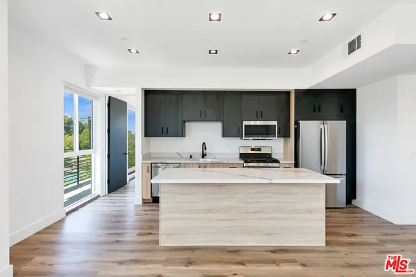 a large white kitchen with kitchen island a stove a refrigerator a sink and a dining table with wooden floor