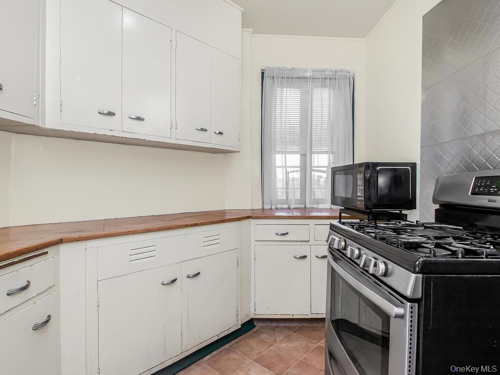 1521 Unionport Road, Unit 11A Bronx, NY 10462 - Photo 5 of 9 Kitchen with gas range, black microwave, white cabinetry, wooden counters, and light tile patterned floors