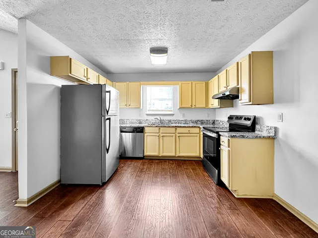 a kitchen with a white cabinets a sink a window a wooden floor and stainless steel appliances