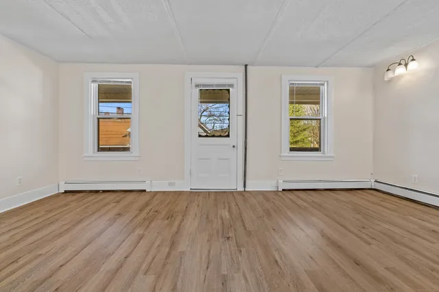 a view of an empty room with window and wooden floor