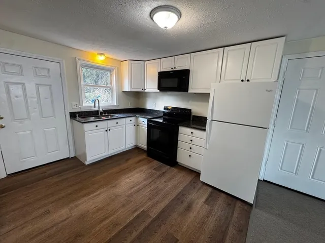 a kitchen with granite countertop a refrigerator a sink dishwasher a stove and white cabinets with wooden floor