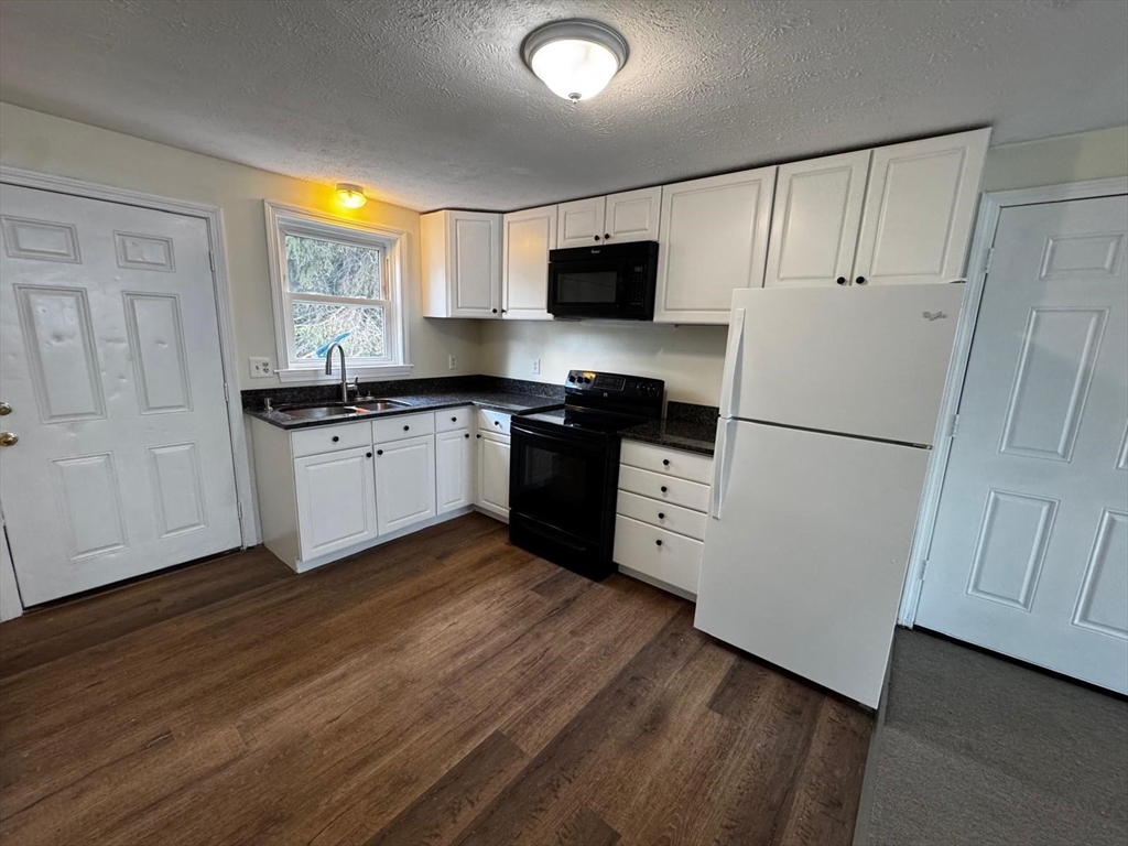 a kitchen with granite countertop a refrigerator a sink dishwasher a stove and white cabinets with wooden floor