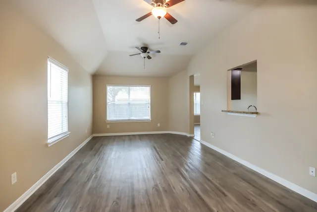 an empty room with wooden floor chandelier fan and windows