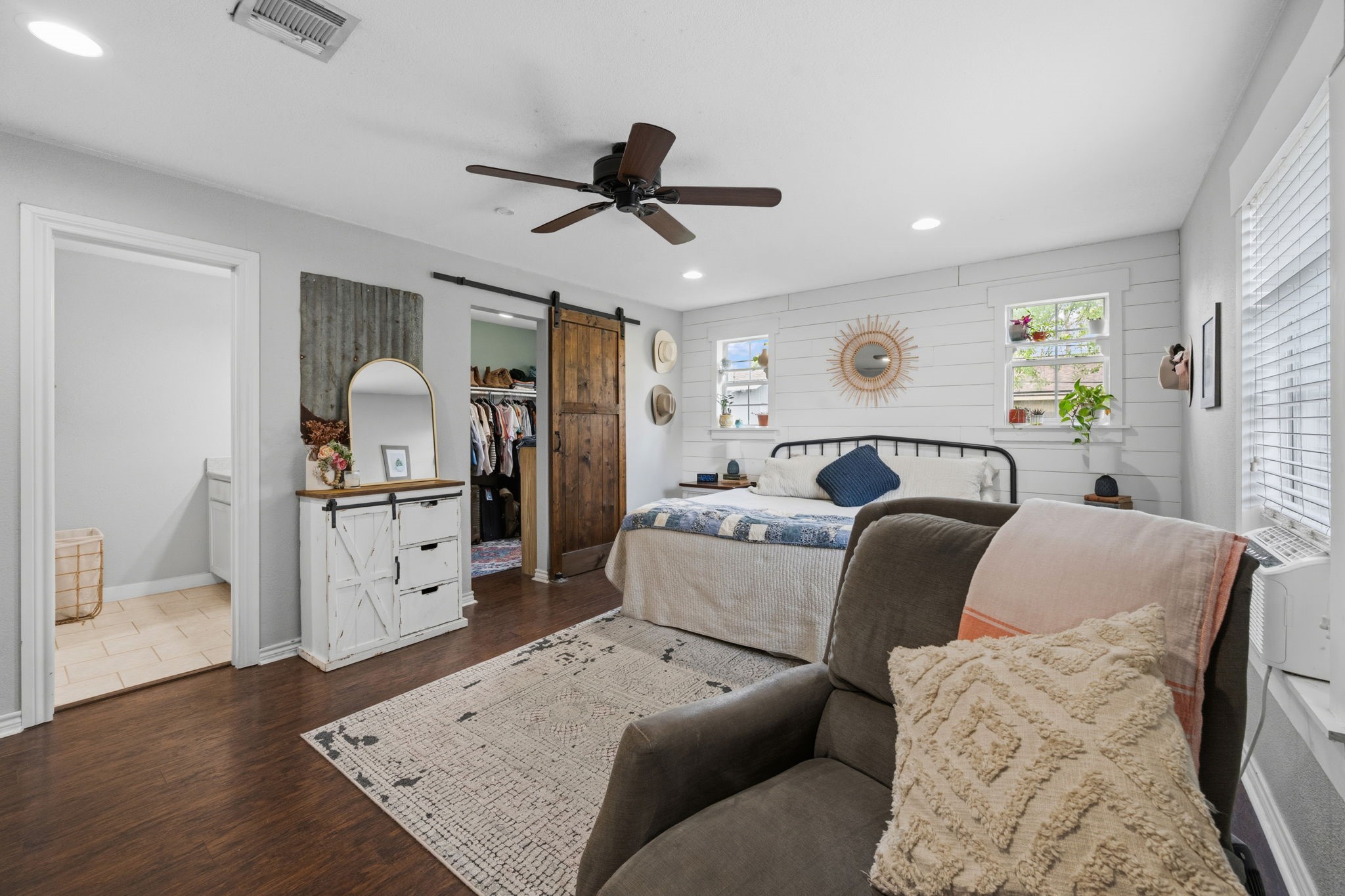 431 Corydon Drive Houston, TX 77336 - Photo 16 of 26 Spacious primary bedroom with laminate wood flooring, a ceiling fan, and abundant natural light. A rustic sliding barn door adds charm, while a cozy seating area and private en-suite bath complete the space.