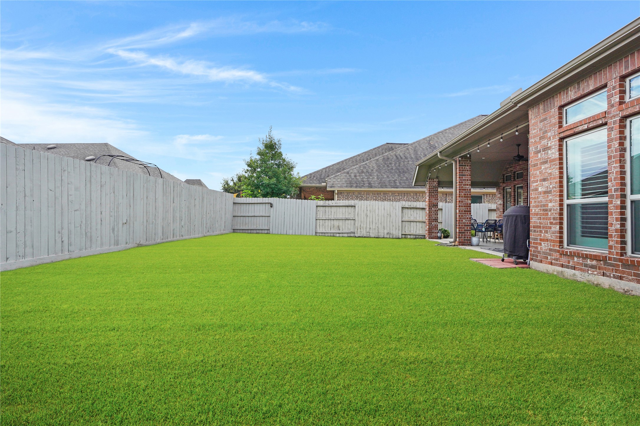 2345 Redwood Ridge Trail Manvel, TX 77578 - Photo 38 of 39 Spacious backyard with well-maintained green lawn, bordered by a wooden privacy fence. The brick exterior features large windows, and there's a covered patio area perfect for outdoor gatherings.