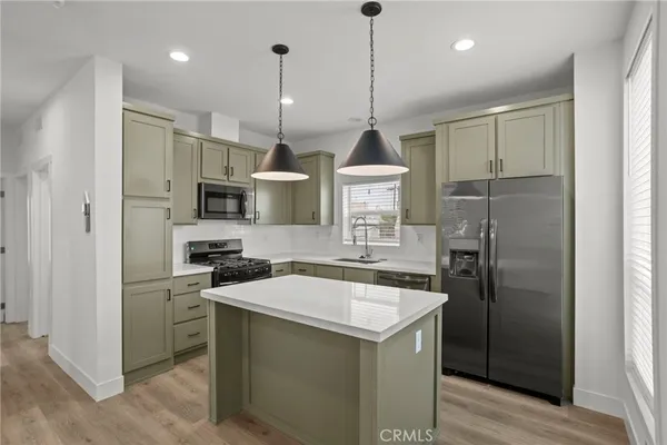 a kitchen with stainless steel appliances granite countertop a sink a stove a refrigerator and island with wooden floor